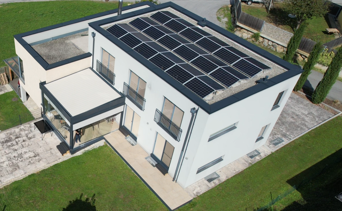 Luftaufnahme eines modernen weißen Wohngebäudes mit Flachdach und darauf aufgeständerten Photovoltaik-Modulen